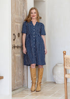 Woman wearing navy blue based white striped print 100% cotton dress with, relaxed fit, empire waistline and elasticated elbow length sleeves