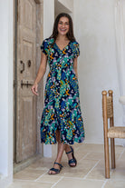 Woman standing backwards in blue based floral midi length rayon button through dress with V-neckline and elasticated waistband