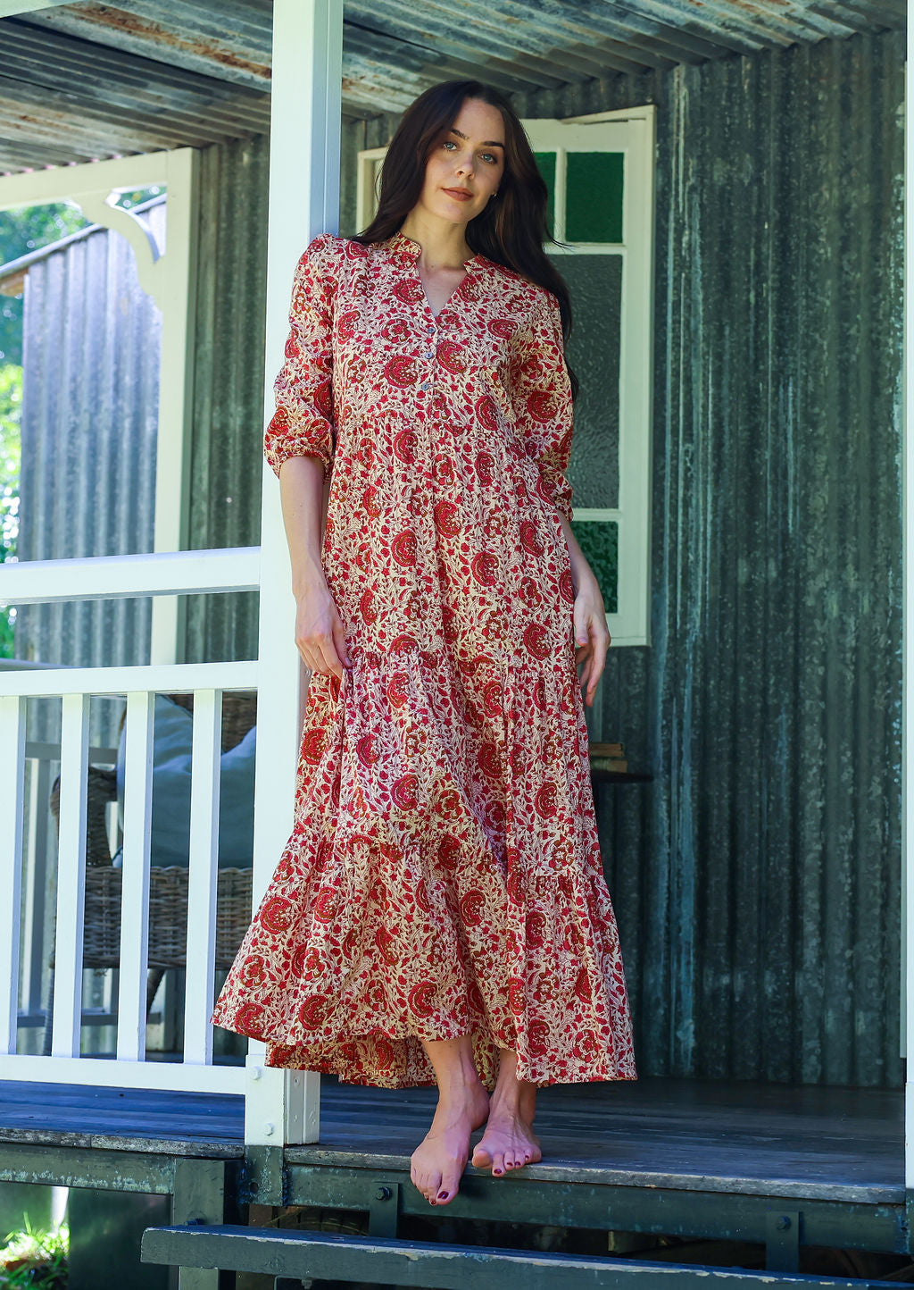Woman standing in cream based 100% cotton flowy tiered maxi dress with 3/4 sleeves, buttoned bodice and pockets 