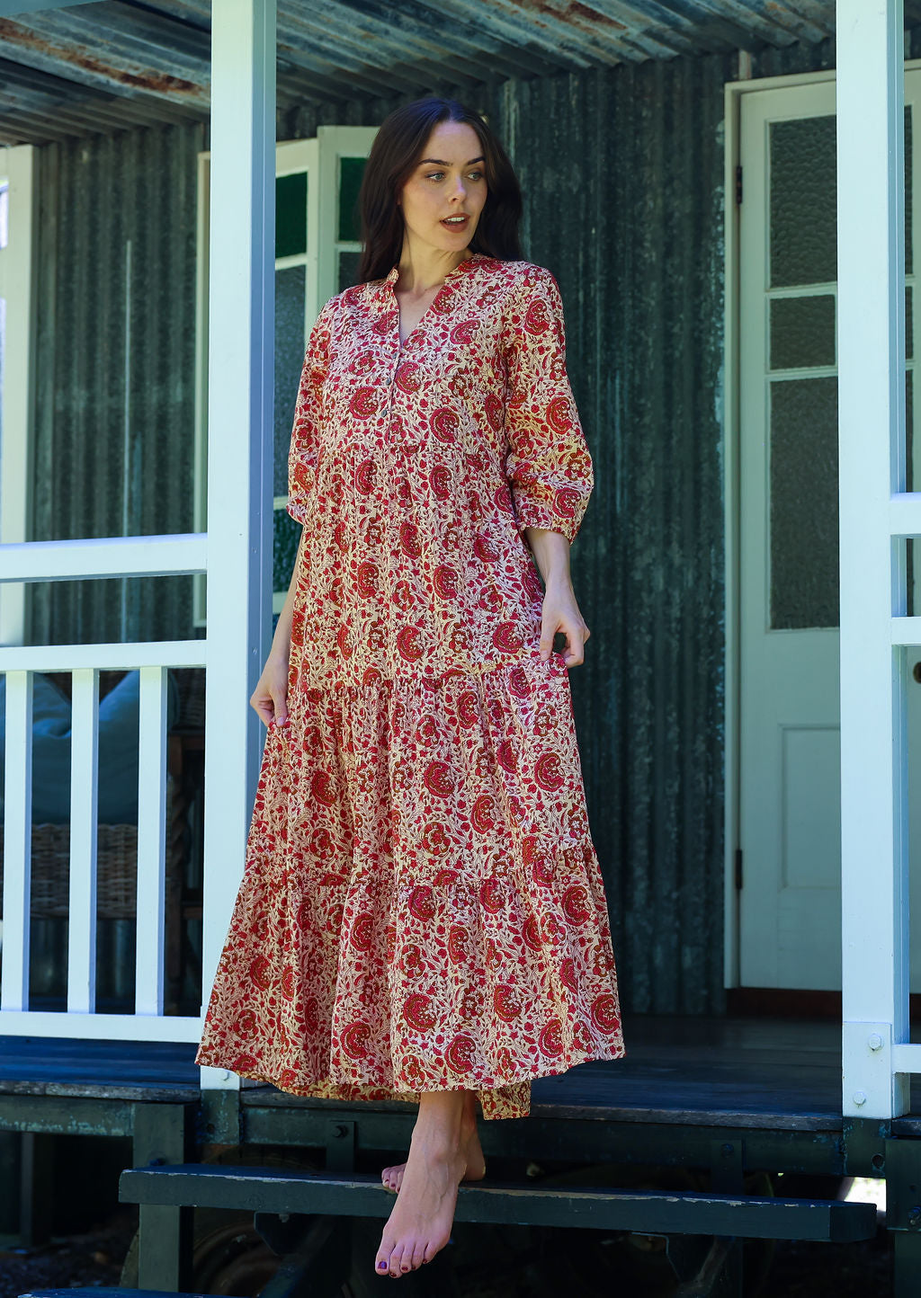 Woman poses in cream based floral cotton maxi dress with buttoned bodice, 3/4 sleeves and flowy three tiered maxi skirt