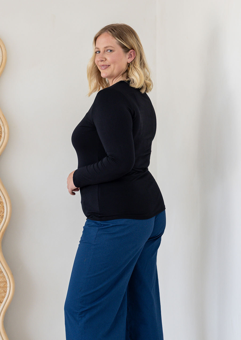 A woman with blonde hair is shown from a side-back angle wearing a black long-sleeve rayon jersey top and blue wide-leg pants