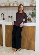 Woman leaning on a kitchen bench wearing a dark brown rayon jersey long-sleeve top with a round neckline and black pants