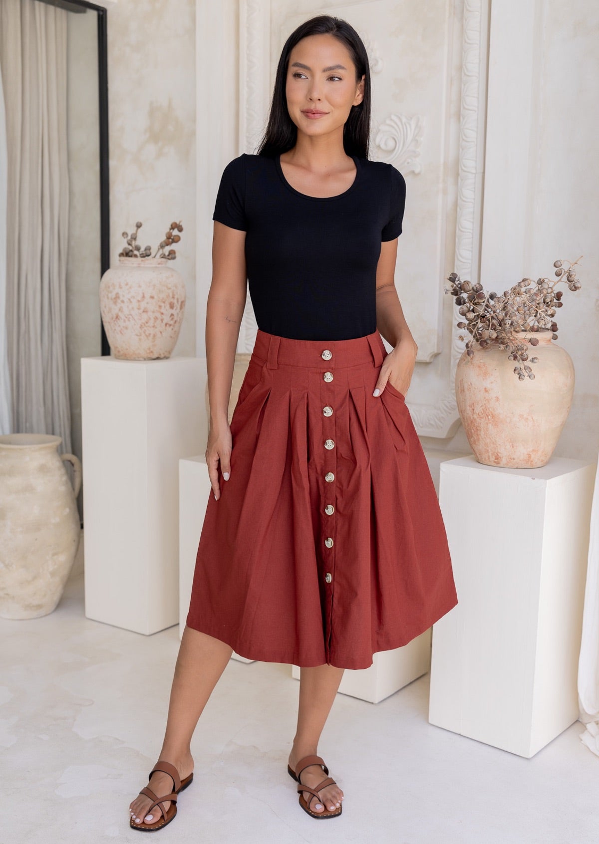 Woman wears rust coloured cotton A-line button through skirt that sits over knee, paired with a black t-shirt