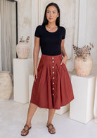 Woman wears rust coloured cotton A-line button through skirt that sits over knee, paired with a black t-shirt