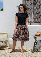 Woman wearing a basic black top and knee length button through cotton skirt with box pleats belt loops and pockets 