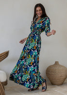 A woman swishes navy blue rayon maxi dress with 3/4 sleeves, buttoned bodice and wide shirred waistband, in a colourful floral and peacock print
