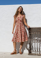 Model wearing a knee length 100% cotton dress in cream based floral print with scoop neck, pockets and cap sleeves 