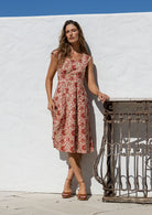 Woman in a floral dress standing against a white wall with a metal gate.