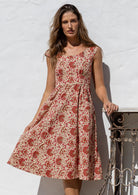 Model flaunting a knee length 100% cotton dress in cream based floral print with scoop neck, pockets and cap sleeves