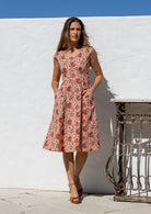 Model in knee length, cream based floral 100 percent cotton scoop neck retro style dress with pockets and cap sleeves 