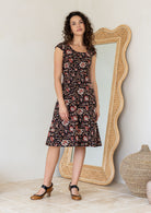 Model wearing a Indian traditional print dress with scoop neck, cap sleeves and piped detailing at the waist and pockets.