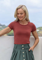 Woman wearing a terracotta shirt and green skirt with a scenic background