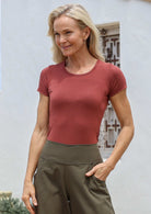 Woman wearing a terracotta shirt and green pants against a light background