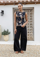 Woman holding the bottom hem of sleeveless black based floral top paired with black pants