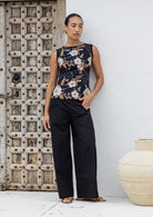 Woman wearing a sleeveless top with a black based floral print, paired with black plain pants 