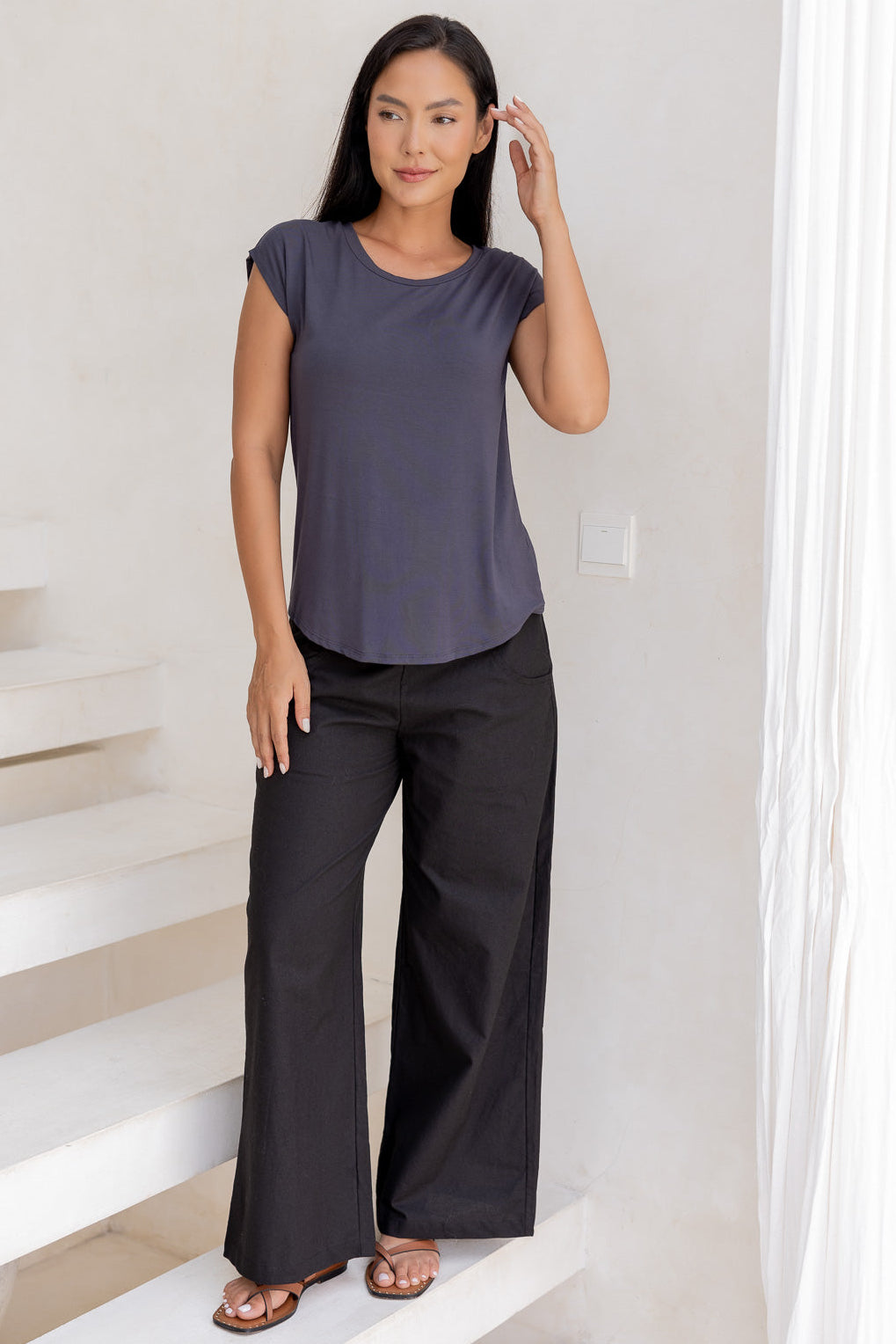 Woman wearing a 100% rayon dark grey top and black pants standing in a room with white walls and a staircase.