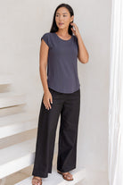 Woman wearing a 100% rayon dark grey shell t-shirt and black pants standing on a white staircase.