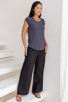 Woman wearing a 100% rayon dark grey shell t-shirt top and black pants standing on a white staircase.