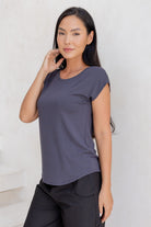 Woman with hand on face wearing a 100% rayon dark grey shell t-shirt and black pants against a white background