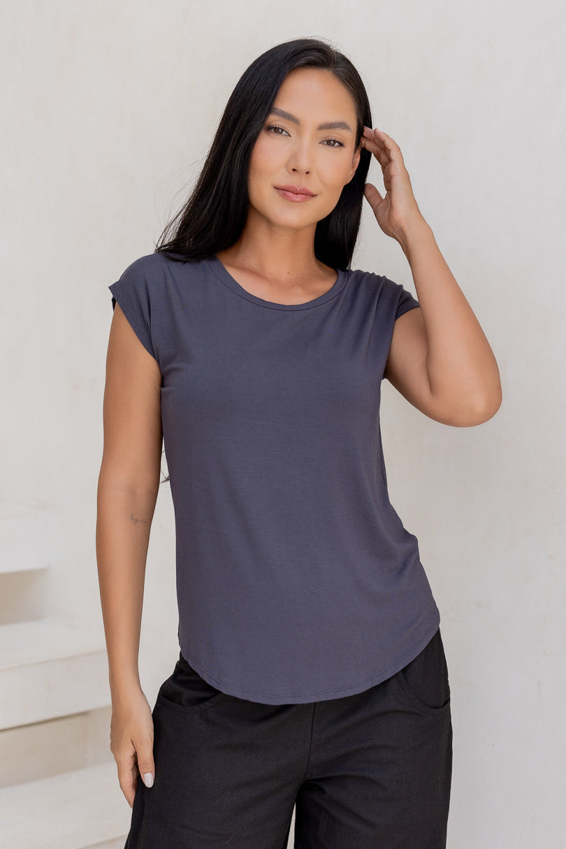 Woman wearing a 100% rayon grey shell t-shirt and black cotton pants against a white wall.