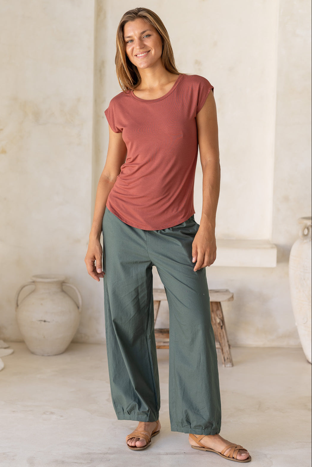 Woman wearing a 100% rayon terracotta shell t-shirt with plain green pants in an indoor setting