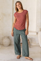 Woman wearing a 100% rayon terracotta shell t-shirt with plain green pants in an indoor setting