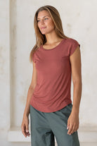 Woman wearing a 100% rayon terracotta shell t-shirt standing against a white wall.
