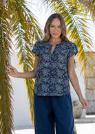 Woman wearing a 100% cotton navy blue based floral blouse and plain pants standing against a white wall.