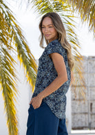 Woman stands sideways wearing a 100% cotton navy blue based floral short sleeve top and plain pants.