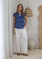 Woman standing wearing a 100% cotton blue based floral top paired with a plain white pants