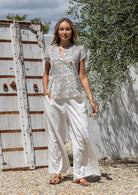 Woman standing wearing a 100% cotton white based floral top paired with a plain white pants