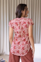 Woman stands backwards wearing a 100% cotton warm gentle cream based floral blouse and plain pants.