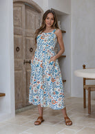 Woman wearing a 100% cotton dress in white based floral print paired with tan sandals.