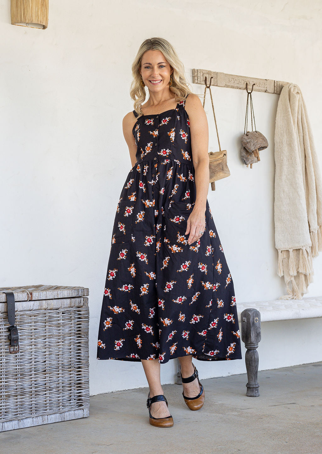 Woman wearing a 100% cotton dress in black based floral print paired with tan sandals.