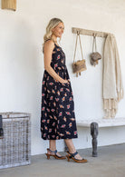 Woman standing sideways wearing a 100% cotton button bodice sleeveless dress in black based floral print