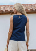 Woman standing in a back pose wearing a 100% cotton sleeveless sea blue top with high round neckline and a keyhole button at the nape of neck