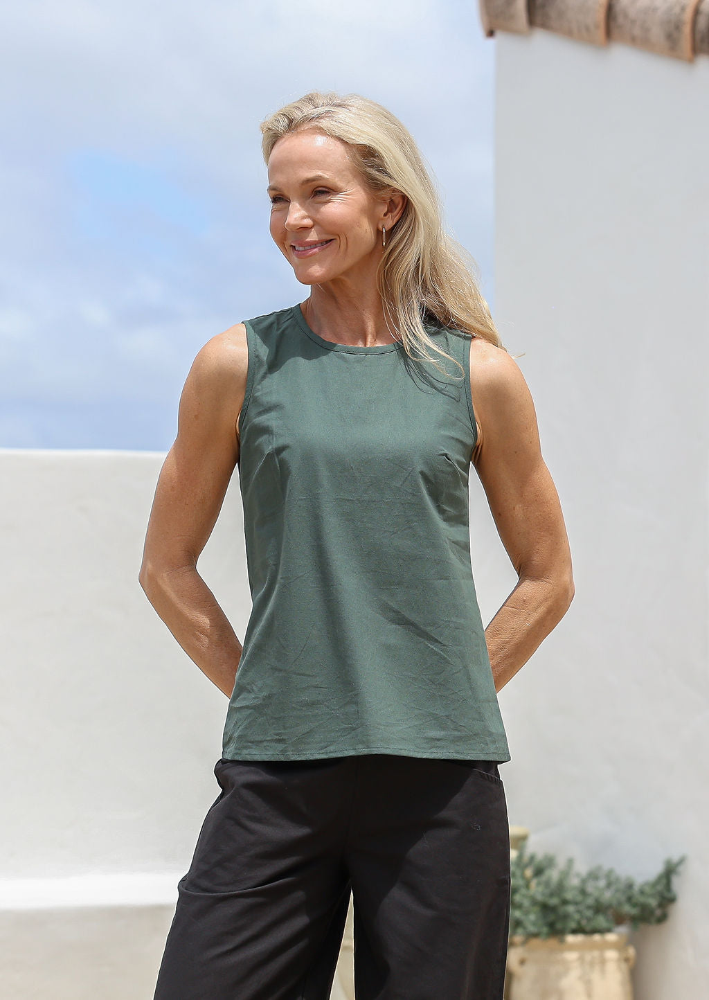 Woman wearing a green sleeveless cotton top with side bust darts and piped detailing at round neckline and armholes