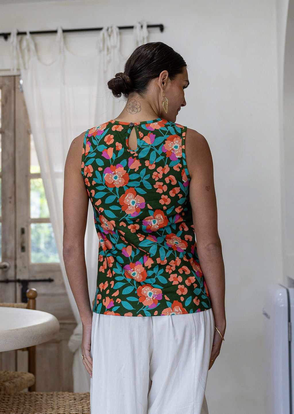 Woman standing backwards wears 100% cotton floral top, sleeveless design. 