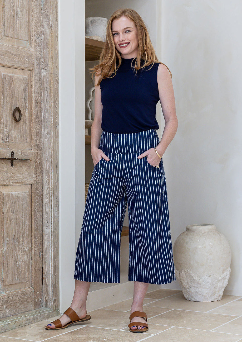 Model standing wearing a 100% cotton capri style wide leg pants in navy based white striped print and side pockets
