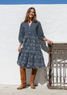 Woman poses in cotton tiered over the knee dress with 3/4 sleeves, buttoned bodice and V-neckline
