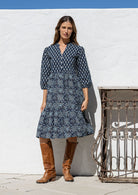 Woman wearing a 100% cotton tiered over the knee dress with 3/4 sleeves, buttoned bodice and V-neckline