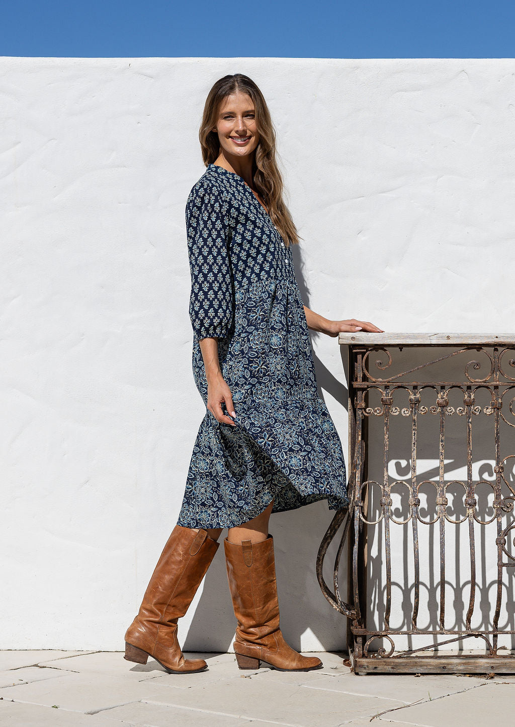 Model stands side on in cotton over the knee length relaxed fit dress with 3/4 sleeves, paired with brown boots.