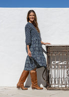 Model stands side on in cotton over the knee length relaxed fit dress with 3/4 sleeves, paired with brown boots.