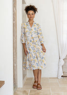 Woman poses in cotton tiered over the knee dress with 3/4 sleeves, buttoned bodice and V-neckline
