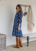 Model stands side on in cotton over the knee length relaxed fit dress with 3/4 sleeves, paired with brown boots.