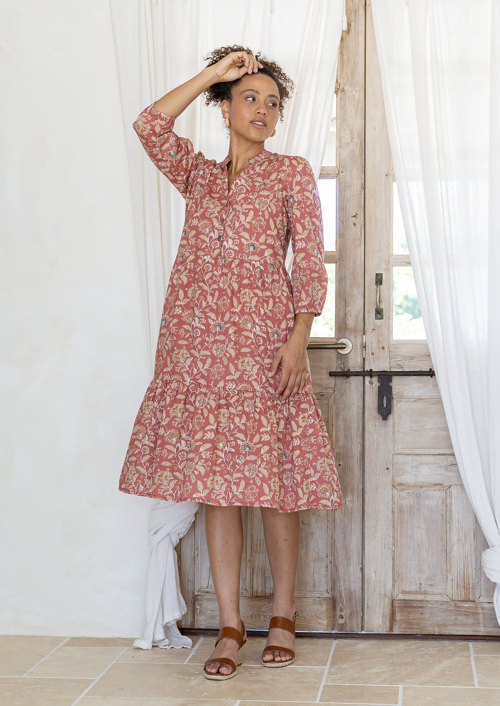 Woman flaunting cotton tiered dress in rose pink floral print, with 3/4 sleeves, buttoned bodice and V-necklin