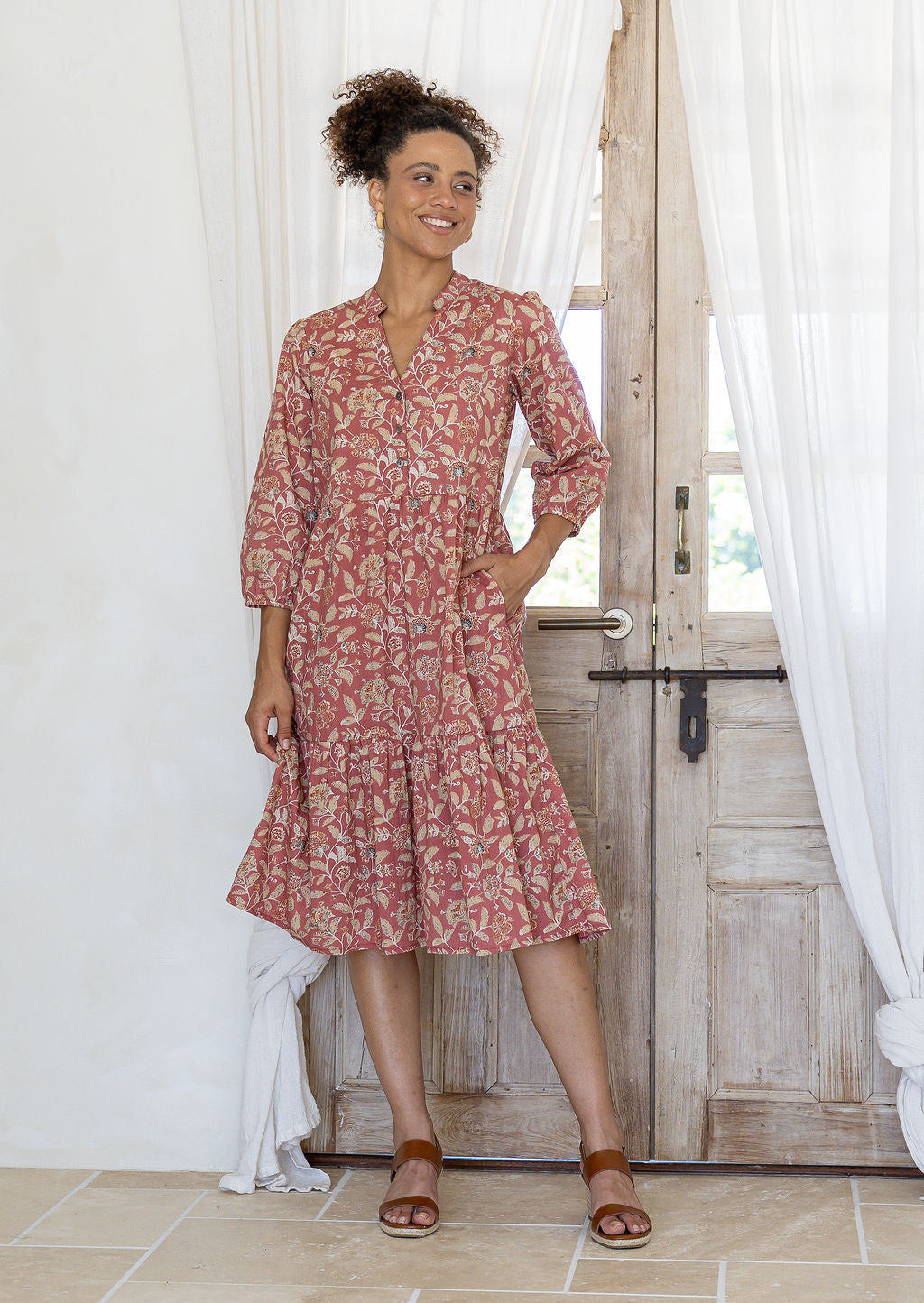 Woman poses in cotton tiered over the knee dress with 3/4 sleeves, buttoned bodice and V-neckline