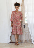 Woman wearing with one hand in pocket of a 100% cotton tiered over the knee dress 3/4 sleeves, buttoned bodice and V-neckline