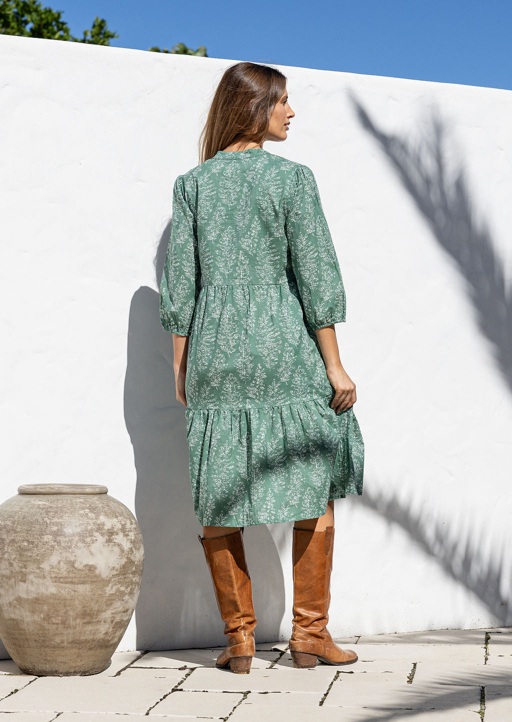 Model stands backwards in cotton over the knee length relaxed fit dress with 3/4 sleeves, paired with brown boots. 