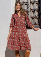 Woman poses in cotton tiered over the knee dress with 3/4 sleeves, buttoned bodice and V-neckline